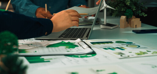 A modern office scene showcases a collaborative meeting focused on sustainability and green solutions, featuring documents, a laptop, and hands actively engaging in discussion. SACTR