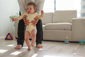 Father helping a baby to learn how to walk. Copy space, background.
