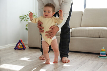 Father helping a baby to learn how to walk. Copy space, background.