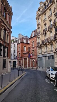 A charming Parisian corner with unique patterned buildings. Classic Haussmann-style architecture with ornate iron balconies lines the street. French National School for the Judiciary (magistrature)