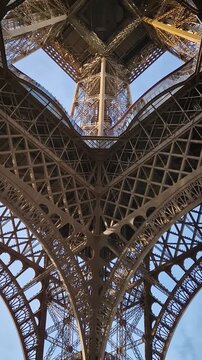 A mesmerizing look up into the intricate iron heart of the Eiffel Tower, through massive lattice arches, revealing the complex geometric engineering and the internal elevators ascending toward the sky