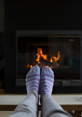 Pies con medias a rayas apoyados sobre mesa y de fondo un hogar a leña con fuego