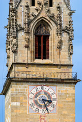Historic clock tower in Bressanone with ornate Gothic stone carvings and a colorful Roman numeral clock, symbolizing medieval architecture and cultural heritage in South Tyrol, Italy.