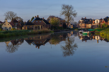 Obraz premium Perfect reflection of the Dutch town Bedum on the canal surface. Traditional brick houses, boats and spring trees in calm morning light