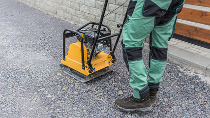 Working with vibro-compaction plate to compact gravel  base bed. Vibrating plate in construction.