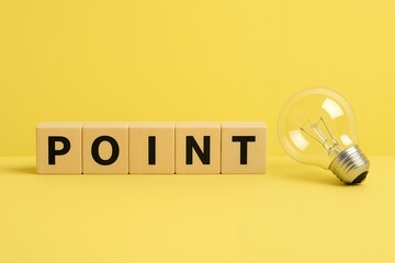黄色背景に並んだPOINTの木製ブロックと電球で重要なポイントやひらめきを強調するイメージ