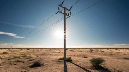 A professional photograph of a solitary electric pole standing tall in a vast dry savanna landscape with scattered grass and minimal vegetation, under the intense glare of bright sunlight.