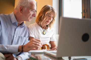 Senior couple calculating budget and managing investments on laptop