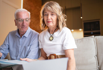 Senior couple sitting on sofa, reading financial documents together at home