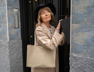 Senior woman looking up, checking mail slot on a city building entrance