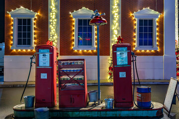 Classic red vintage gas pumps decorated with christmas lights and wreaths in front of a brick building, creating a nostalgic holiday scene ideal for seasonal backgrounds, travel concepts, retro themes © divampo