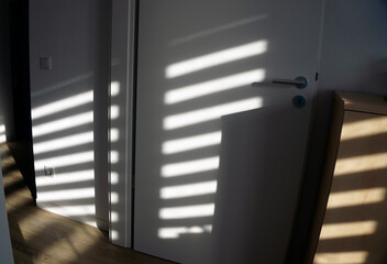 Soft shadow of window frame cast on white door and wall. Sunlight creating geometric light and shadow pattern indoors, minimalist interior detail, cozy home atmosphere still life.