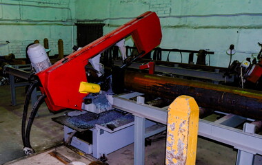 Industrial horizontal band saw cutting large steel pipe in workshop
