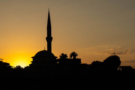 Silhouette of mosque with minaret against vibrant sunset sky. Traditional islamic architecture at golden hour. Time for azan prayer call. August, Mediterranean, Turkey.