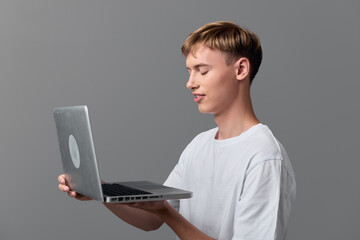 Hands holding a laptop, man in a white tee using a device, technology concept for digital work, focused expression, modern setup, online learning, and creative workflow.