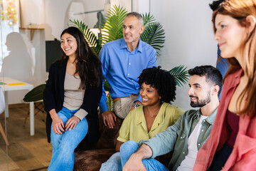 Multi-ethnic business team smiling and listening during an informal office meeting. Diverse colleagues fostering teamwork and collaboration. Business lifestyle and teamwork concept