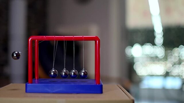 Slow motion footage shows a person playing with a table Pendulum balance balls game indoors.