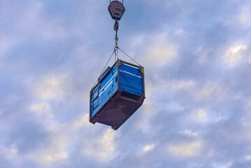 diesel generator hangs high on a crane's hoist block against a dark cloudy sky