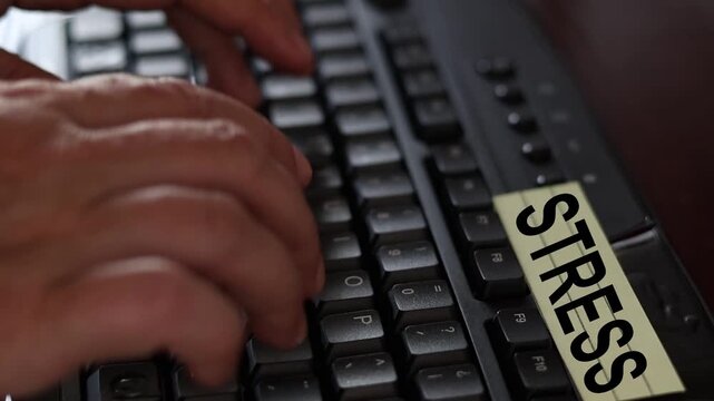 Un primer plano de un teclado de una computadora con las manos de una mujer adulta y una nota amarilla con la palabra estr&eacute;s