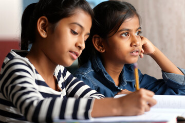 Two schoolgirls studying at a desk, one writing while the other watches thoughtfully in class. Generative AI