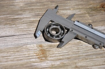 Close-up of vernier caliper measuring ball bearing diameter on wooden background