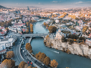 Church on a cliff overlooking the Kura River and Tbilisi city skyline, featuring bridges and a cityscape at sunset © EdNurg