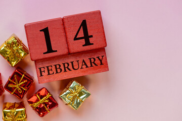 February 14. Valentine's Day composition with a wooden calendar and gift boxes on a pink background. Copy space. Concept of a day of professing love