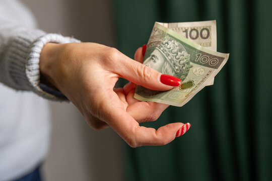 zgięty banknot 100 zł w dłoni kobiety