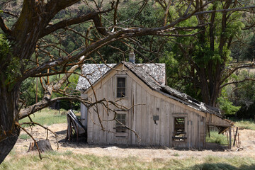 An abandoned home sits among dry grass in a rural farmland area. The house has broken windows and heavy damage.