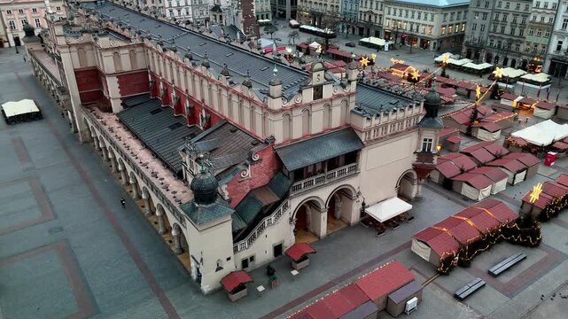Aerial circling shot of the historic Sukiennice Cloth Hall and the empty, closed Christmas Market stalls covering Krakow's Rynek Gł&oacute;wny during a cold winter morning.