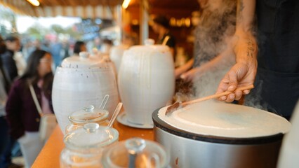 vendor pouring crepe batter while customer watches at stall