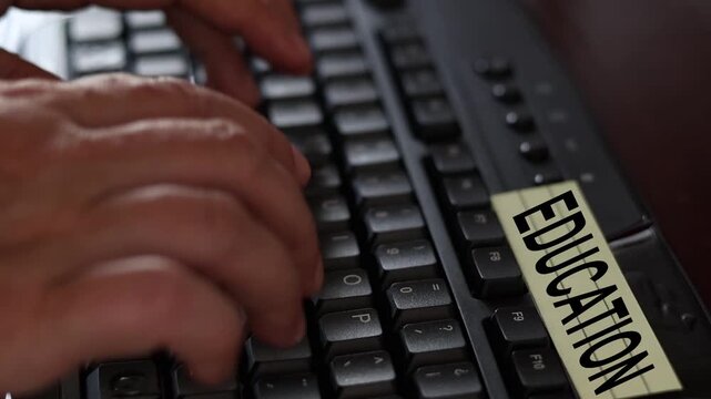 Un primer plano de un teclado de una computadora con las manos de una mujer adulta y una nota amarilla con la palabra educaci&oacute;n