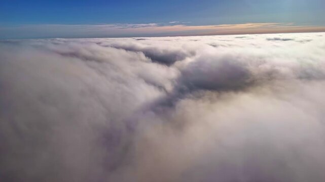 Drone pulls back and shifts right above a dense cloud layer at dawn.