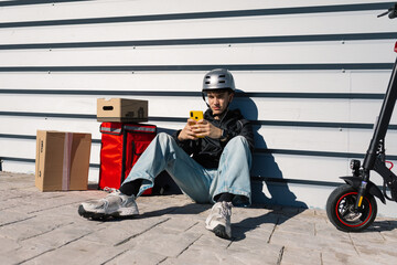 Young delivery boy sitting beside scooter with packages