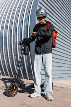 Young delivery boy on electric scooter checking watch