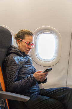 Woman using phone in airplane seat by a window