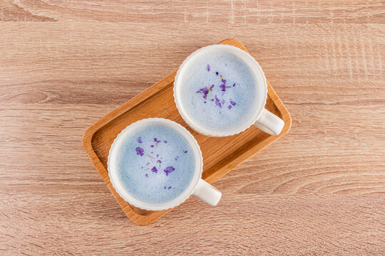 Two cups of herbal blue matcha latte on wooden tray