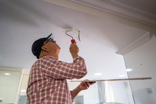 Senior enthusiast painting ceiling in kitchen renovation