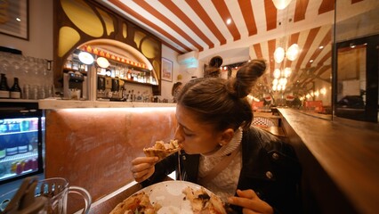Young lady with determined expression consumes massive cheesy slice