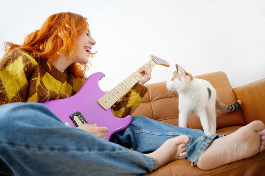 Woman playing guitar with cat on couch