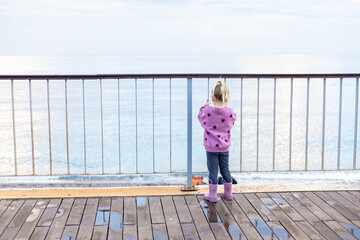 Toddler in purple sweater and boots on wet boardwalk