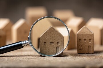 Magnifying glass focuses on a cardboard house amidst other small houses