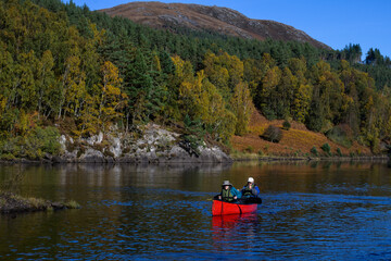 Fall outdoor adventure vacation, senior man and woman paddling a red canoe on lake, Loch Beinn o Mheadhain, in Glen Affric nature reserve, Scotland
