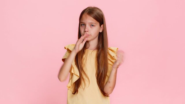 Young child girl shows timeout gesture with tired expression, seriously gazing at camera as if requesting a break. School kid isolated on pink background with emotional and expressive body language.