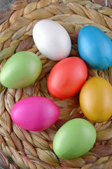 Brightly colored easter eggs, in a straw basket against a natural beige background.