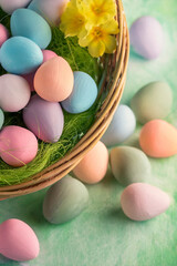 Chocolate painted mini Easter eggs in straw or whicker basket against a green spring background