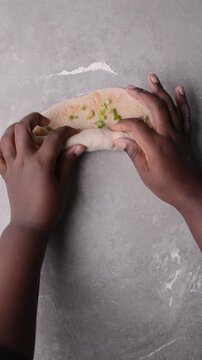 Overhead view of raw chinese scallion pancakes being rolled on grey countertop, top view of homemade scallion pancakes being shaped on countertop, process of making cong you bing