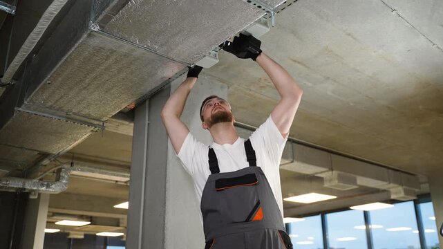 Male electrician installing cable tray on concrete ceiling