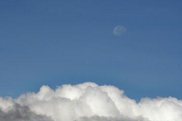 Half moon on a blue sky over white clouds