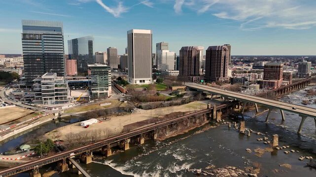 Cinematic aerial view of downtown Richmond Virginia skyline and James River with industrial bridge foreground